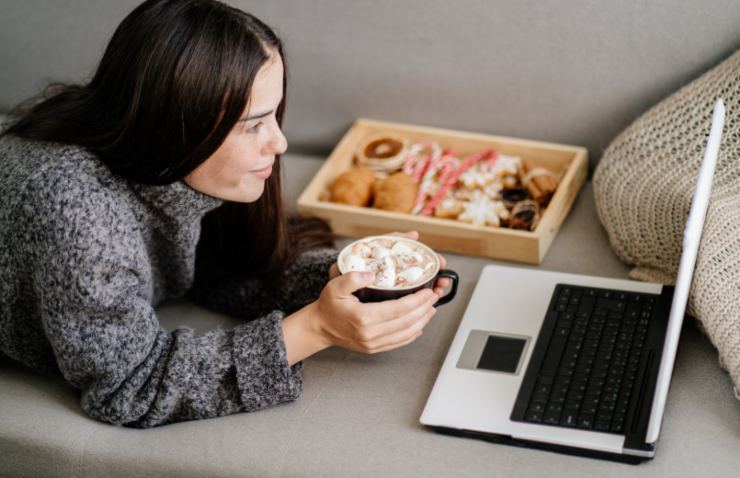 donna che guarda qualcosa sul computer con in mano una bevanda calda e accanto dei pasticcini